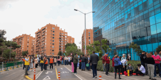Personas reunidas en un espacio público junto a edificios de Bogotá durante una actividad de simulacro de evacuación. Varias personas permanecen organizadas sobre la vía, delimitada con conos de tránsito, mientras personal de apoyo coordina la jornada.