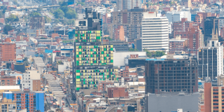 Vista panorámica del centro de Bogotá con edificios de diferentes alturas, una torre de fachada verde y amarilla en primer plano, vías urbanas y construcciones residenciales y comerciales densamente agrupadas.