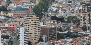 Vista panorámica de Bogotá con edificios residenciales y comerciales de diferentes alturas en primer plano, y los Cerros Orientales en un día nublado.