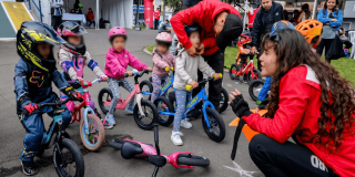 Niños y niñas de primera infancia participan en una actividad de push bike con bicicletas de equilibrio y cascos de protección en un espacio al aire libre en Bogotá.