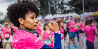Participante de la Carrera de la Mujer con camiseta rosada y audífonos alrededor del cuello, entre corredoras reunidas en la zona de encuentro previa a la competencia.