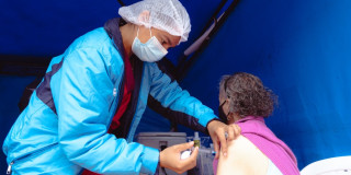 Foto que muestra un enfermero colocando una vacuna en un brazo a una mujer mayor.
