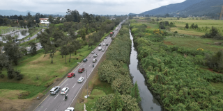 Vista aérea de la Autopista Norte de Bogotá con tránsito vehicular junto a un canal de agua y amplias zonas verdes que serán atendidas por el PMU.