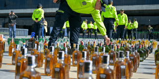 Foto de policías exponiendo en el piso botellas incautadas.