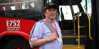 Persona con gorra negra, camisa azul claro y morral gris se encuentra junto a la puerta abierta de un bus rojo del sistema de transporte. En el costado del vehículo se observa la identificación “E752” y el nombre “Gmóvil S.A.S.”, mientras que el interior del autobús muestra pasamanos y escalones amarillos.