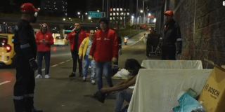 Operativo nocturno de atención social en un corredor vial, con personal de entidades distritales y varias personas junto a enseres y objetos retirados del espacio público.