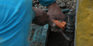 Foto que muestra unas manos con una llave arreglando un tubo de agua