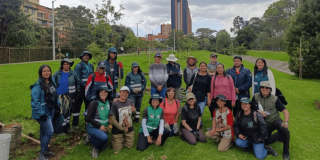 Grupo de personas posa para una fotografía al aire libre sobre una zona con césped. Varias personas llevan chalecos, gorras y prendas de colores llamativos, mientras algunas sostienen herramientas utilizadas en actividades de jardinería o mantenimiento vegetal.