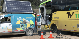 Vehículo de la Unidad Móvil de Control Ambiental de la CAR Cundinamarca, equipado con panel solar en el techo, conectado a un bus de transporte mediante cables de medición.