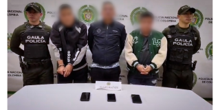 Foto de tres hombres capturados por la policía, escoltados por dos oficiales, uno en cada costado. 