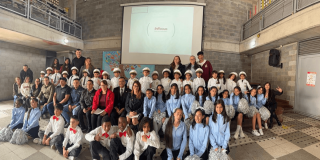 Grupo de estudiantes y docentes de Teusaquillo posa para una fotografía grupal en un espacio interior de un colegio. Al fondo se observa una pantalla de proyección y un muro de ladrillo, mientras los participantes están ubicados en varias filas frente a la cámara