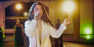 Imagen de una mujer joven de cabello rubio largo cantando con un micrófono.