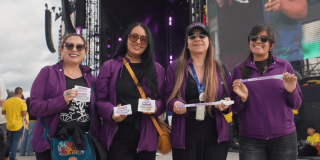 Cuatro mujeres con chaqueta morada de la Secretaría de la Mujer en un concierto.