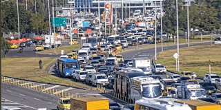 Alta congestión vehicular en avenida El Dorado de Bogotá con filas de carros, buses, camiones y motocicletas avanzando lentamente entre varios carriles. Se observan separadores viales, señalización y tránsito denso en ambos sentidos.