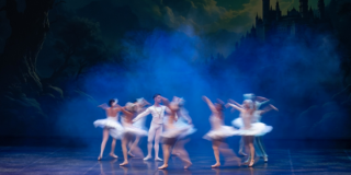 Imagen de una puesta en escena de ballet en la que participan varias mujeres vestidas de blanco y un hombre.