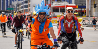 Personas disfrazadas de personajes de anime y superhéroes participan en una jornada de Recreovía en Bogotá, mientras recorren una avenida en bicicleta junto a decenas de ciclistas.