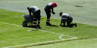 Tres trabajadores realizan labores de mantenimiento y reparación del césped en la cancha del estadio El Campín de Bogotá, junto a la línea lateral del campo de fútbol.