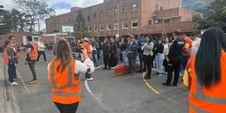 Grupo de personas reunidas en una cancha deportiva durante un ejercicio de simulacro en Bogotá. En primer plano, varias personas usan chalecos reflectivos naranjas mientras orientan a los participantes.