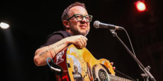 Imagen del cantante César López en un escenario donde lleva una guitarra en sus manos.