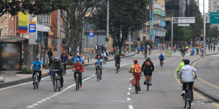 Ciclistas y peatones transitan por una vía de la Ciclovía de Bogotá, rodeados de árboles y edificaciones urbanas durante una jornada recreativa al aire libre