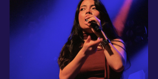 Imagen de una mujer joven que canta con un micrófono en su mano.