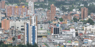 Vista panorámica de un sector urbano de Bogotá con edificios residenciales y comerciales de diferentes alturas, una vía principal con tráfico vehicular y construcciones densamente distribuidas en el paisaje urbano.