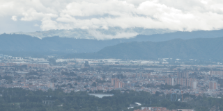 Vista panorámica de Bogotá desde un punto elevado. En primer plano se observan edificaciones urbanas y, al fondo, una cadena montañosa bajo un cielo con abundante nubosidad.
