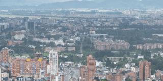 Vista panorámica de Bogotá desde un punto elevado. En primer plano se observan edificios residenciales y comerciales, mientras al fondo se extiende la ciudad bajo un cielo nublado con montañas en el horizonte.