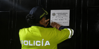 Foto que muestra una policía colocando un aviso de suspension en una reja negra