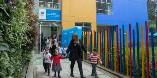 Una mujer rubia agarra de la mano a tres niños pequeños, mientras salen de un edificio azul con amarillo.