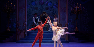 Una mujer y un hombre con trajes de baile, dándose la mano, con un pie levantado 