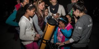 Varios niños y adultos alrededor de un telescopio observando hacia el cielo.