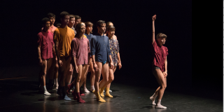 Un grupo de varias personas de pie, una mujer al frente con el brazo extendido 