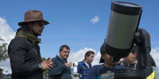 Un hombre enfrente de un telescopio, detrás hay varias personas en fila
