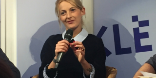 Mujer rubia sostiene un micrófono y conversa.