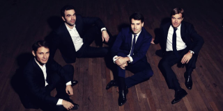 Cuatro hombres sentados en el piso sonríen a la cámara.