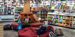 Varias personas sentadas leyendo libros rodeadas de varios estantes de libros 