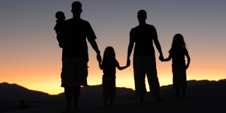 Una familia tomada de manos, al fondo un atardecer.
