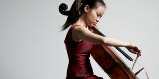 Una mujer joven, de rasgos asiáticos y pelo castaño toca el violonchelo.