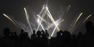 Plano general de un show pirotécnico con muchas personas viéndolo.