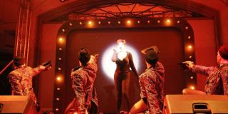 Un grupo de cuatro hombres y una mujer en medio de una puesta en escena en una teatro.