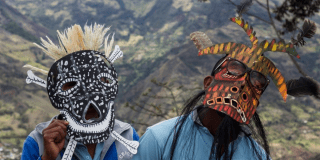 Imagen de dos hombres disfrasados luciendo sus máscaras, al fondo se ve paisaje y montañas