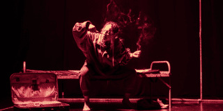 Imagen de mujer jóven sentada en una cama de reclusorio con algo en las manos que emite humo