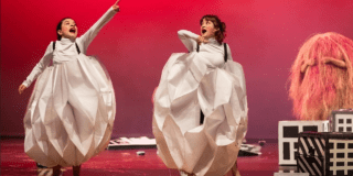 Imagen de dos mujeres jóvenes con trajes blancos y a su lado Burí, un personaje peludo de color rosado