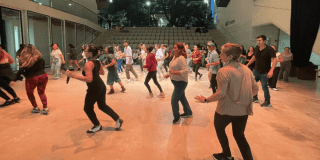 Imagen de un gran salón donde hay muchas personas tomando clases de baile 