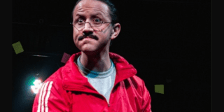 Imagen de hombre mayor que usa gafas y chaqueta roja con cara de angustia con un fondo oscuro