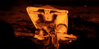 Imagen en fondo oscuro de dos mujeres, una acostada y otra de rodillas con un muñeco que representa la muerte