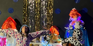 Imagen de los personajes de la obra en tarima donde se aprecia una mujer y un hombre en pijama con animales en peluche a su alrededor