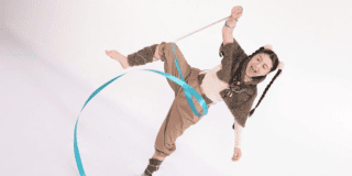 Imagen de una niña vestida de color café claro que juega con unas cintas de colores enredadas en sus manos