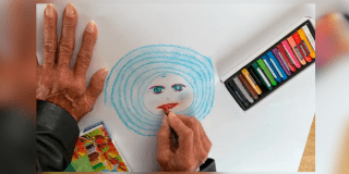 Imagen de una mano de una persona mayor que dibuja una cara con circulos de color azul.